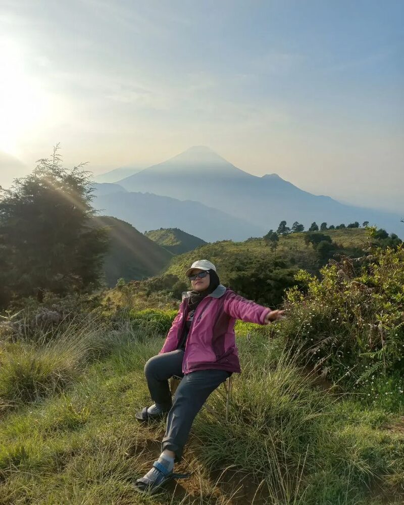 Penyewa duduk di kursi lipat di lereng bukit saat matahari terbit, dengan puncak gunung di kejauhan