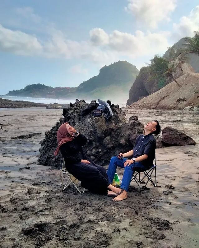 Sepasang penyewa bersantai di kursi lipat di pantai berbatu saat pagi