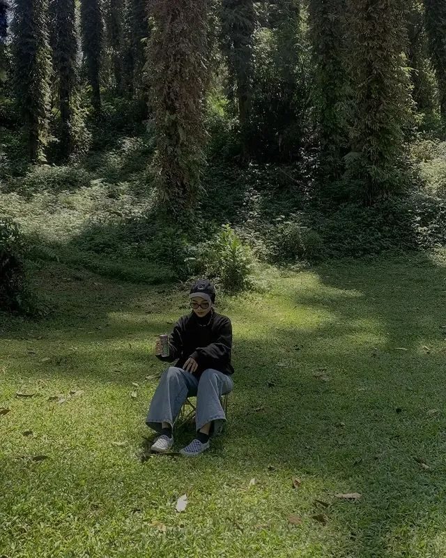 Seseorang duduk sendiri di kursi lipat di tengah hutan berlumut