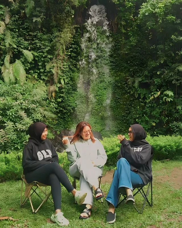 Tiga orang mengobrol di kursi lipat dengan air terjun di belakangnya
